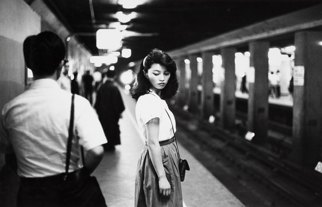 Zwart/wit foto van een Japans vrouw die op het metrostation staat.